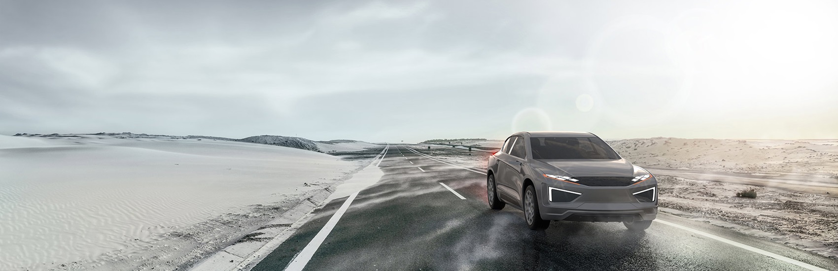 Grey vehicle driving along a road in the desert with overcast sky in background